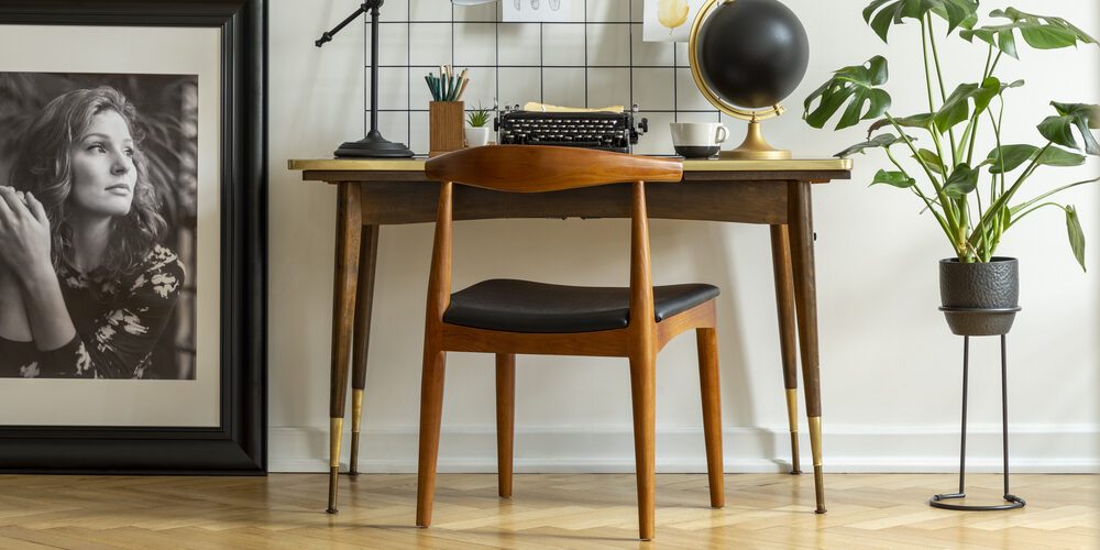 Mid-century modern chair with leather seat by a desk with an industrial lamp and a retro typewriter in a white home office interior